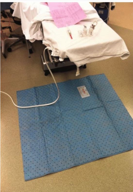 Hospital bed with a blue underpad on the floor beside it.