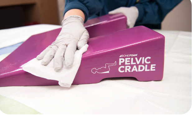 Person cleaning a purple pelvic cradle medical device with a white cloth.