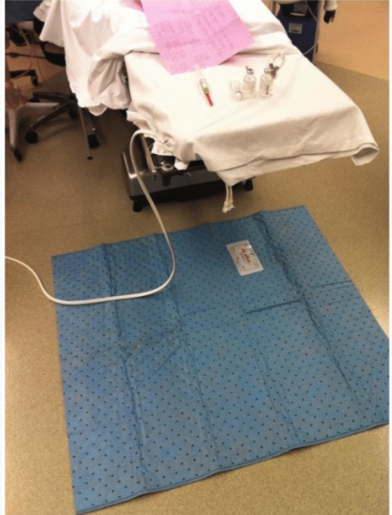 Medical bed with blue disposable sheet on the floor beside it.