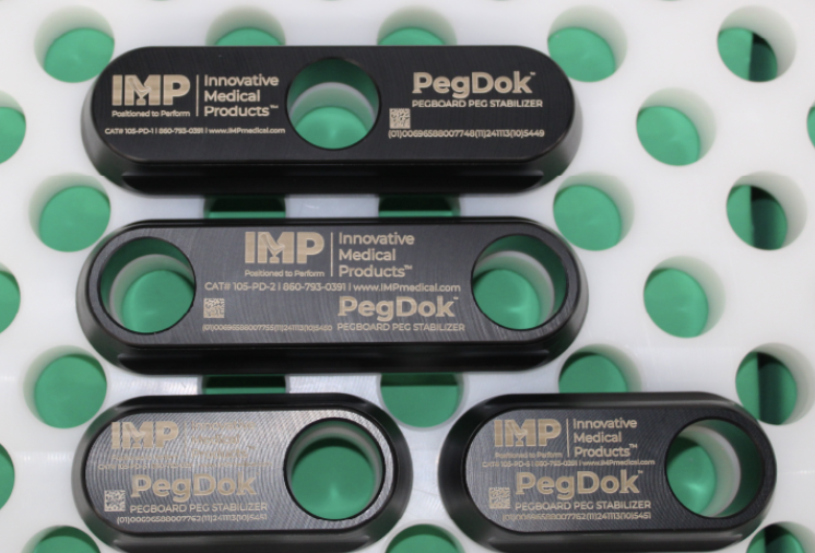 Three black metal PegDok tools with circular openings on a white surface with green dots.