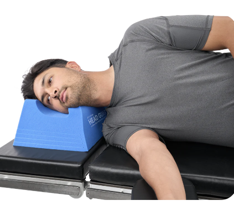 Man lying on a therapy table with a blue neck support pillow.