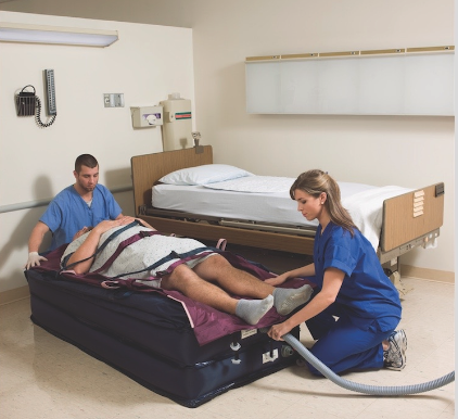 Healthcare worker assisting patient with leg therapy in a hospital room.