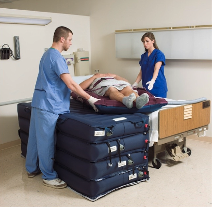 Healthcare workers assisting patient with mobility aid in hospital room.