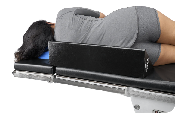 Person lying face down on a treatment table with a black cushion.