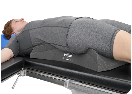 A person lying on a medical imaging table with a positioning cushion under their lower back.